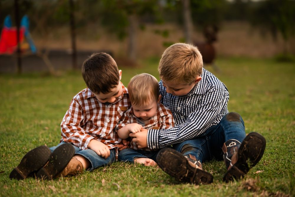 Three children sitting together on grass sharing a playful moment.