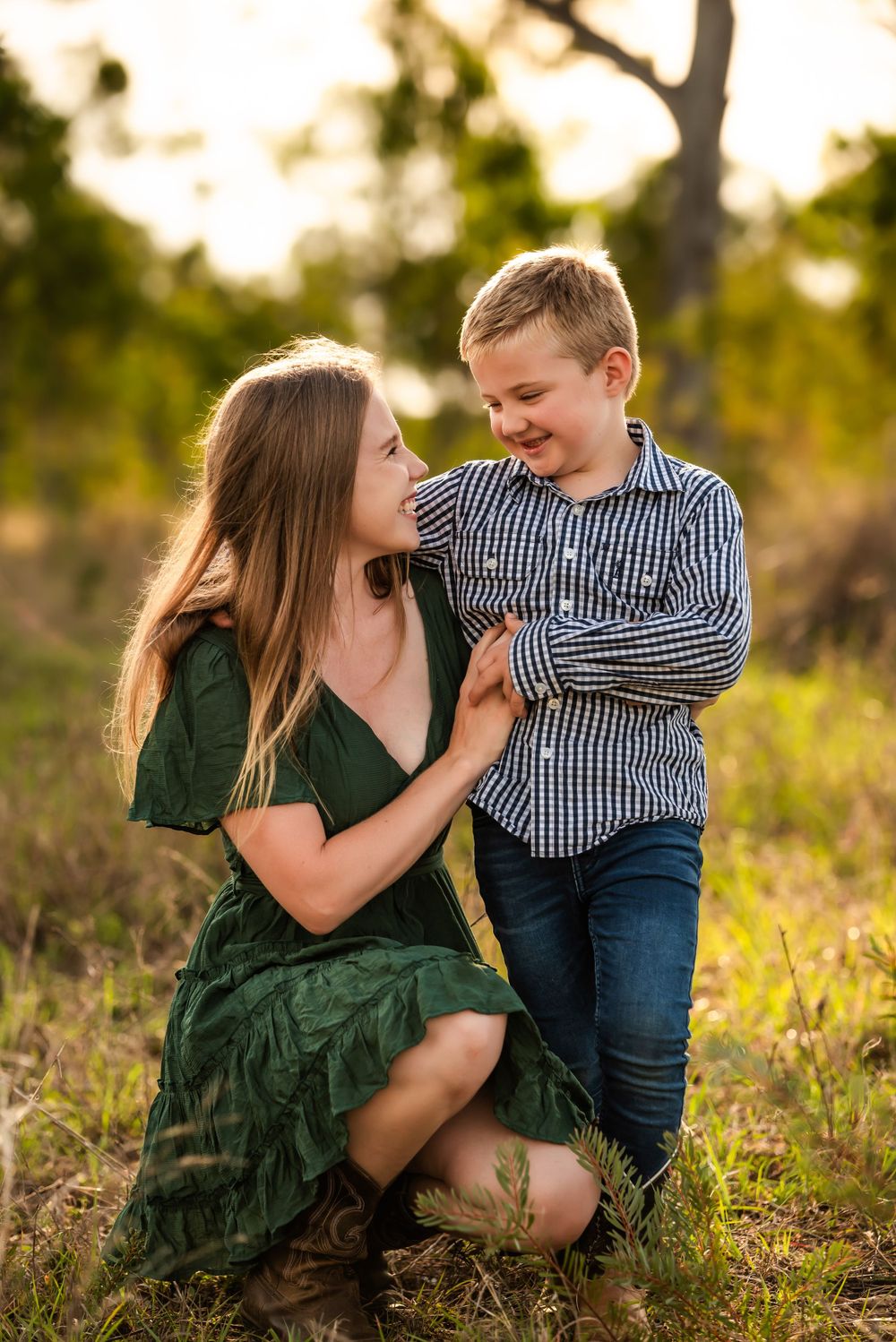 A tender outdoor family moment captured in warm sunlight with a green dress and plaid shirt against a natural setting.