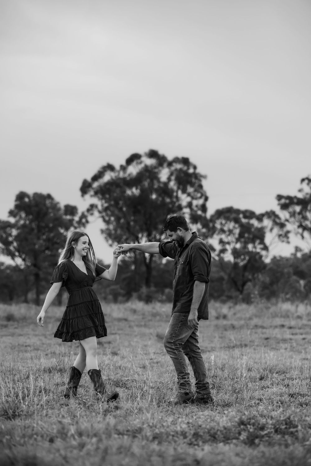 Artistic black and white photo of a couple in a playful outdoor scene with eucalyptus trees.