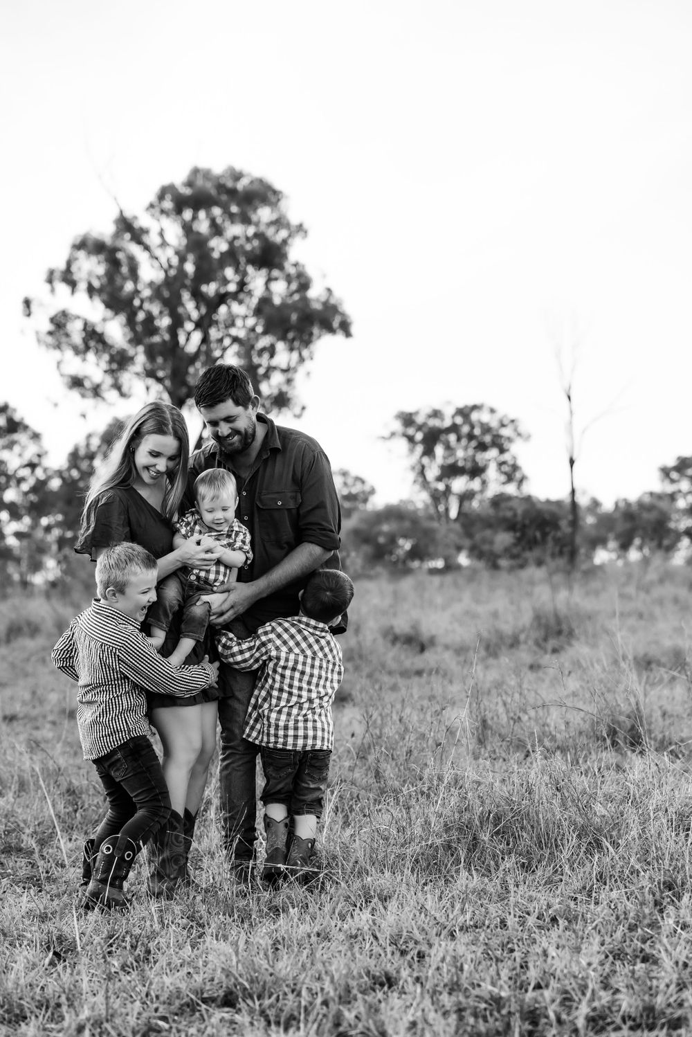 A black and white outdoor family portrait showing playful interaction in a rural field setting.