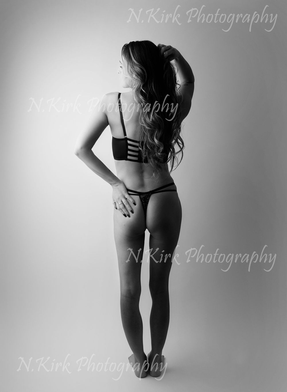 Boudoir image on light backdrop, showing confident pose with lovely shadows and contrasting light.