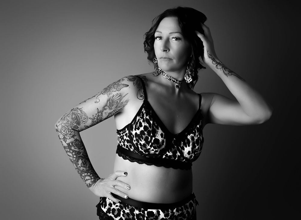 Black and white boudoir  session. Model in leopard print bra and pants, hand on her hip with the other at the side of her hair.