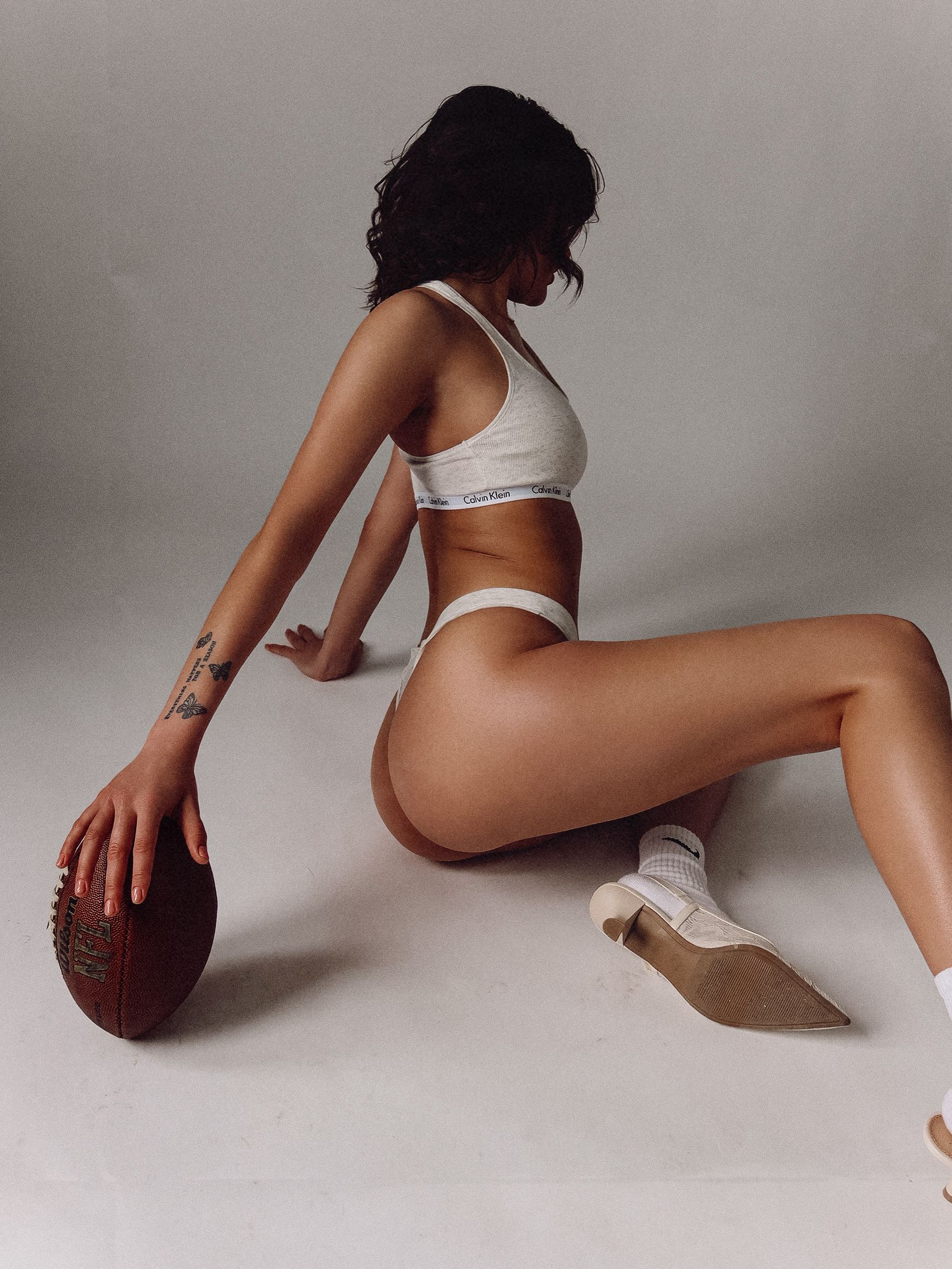 Cropped view of person in white sports bra and socks with football against grey background.