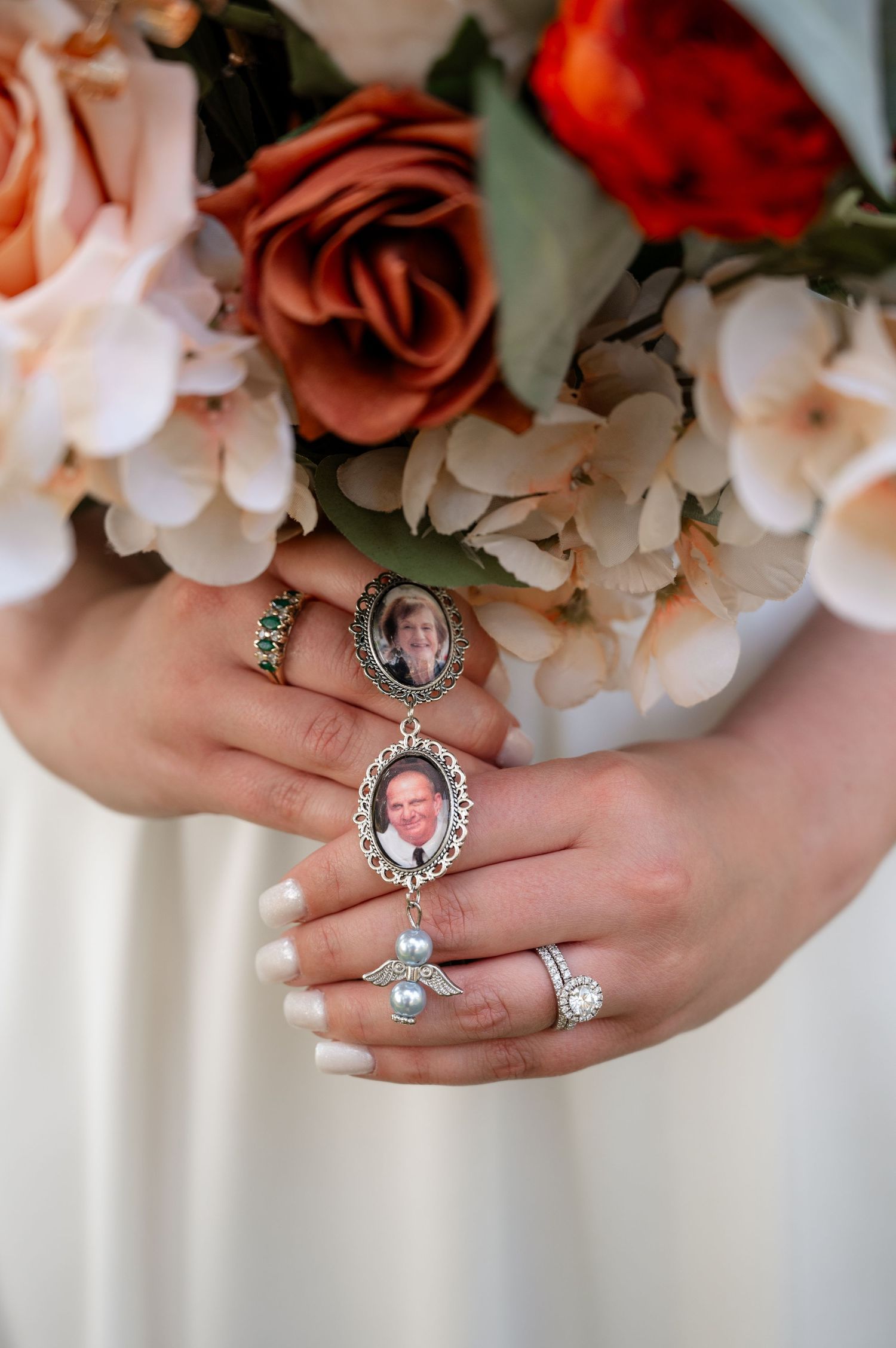 Bride holding memorial photo charms on wedding bouquet with white and terracotta roses.