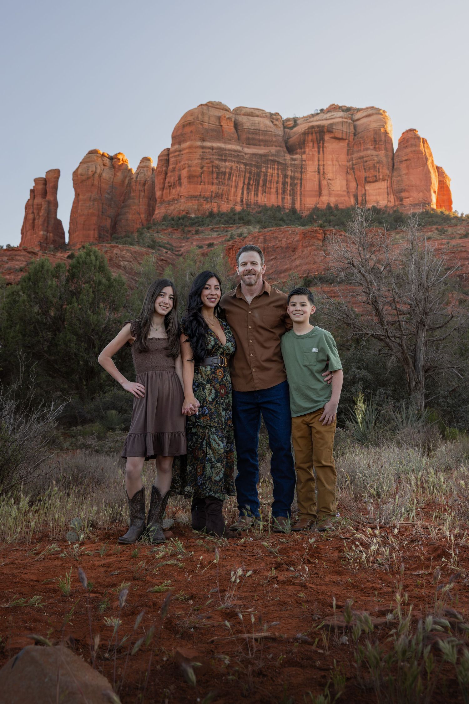 A family of four smiles together in front of Cathedral Rock in Sedona, Arizona at sunset.