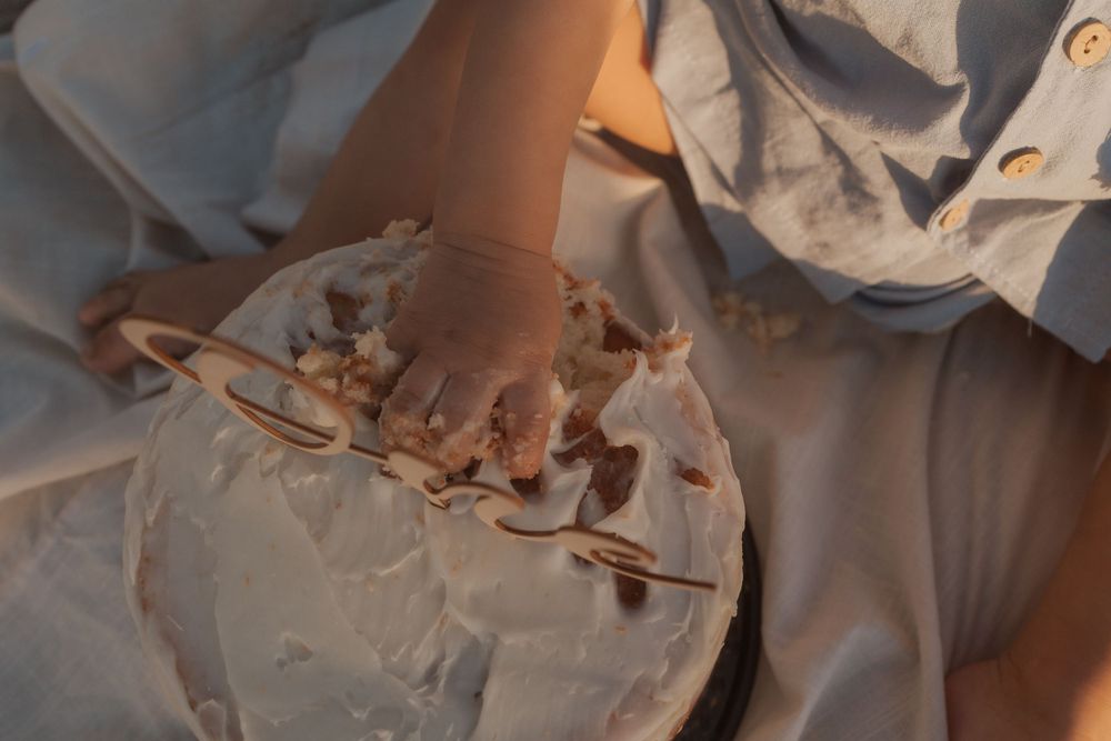 Small toddler hand touching frosting on white decorated cake.