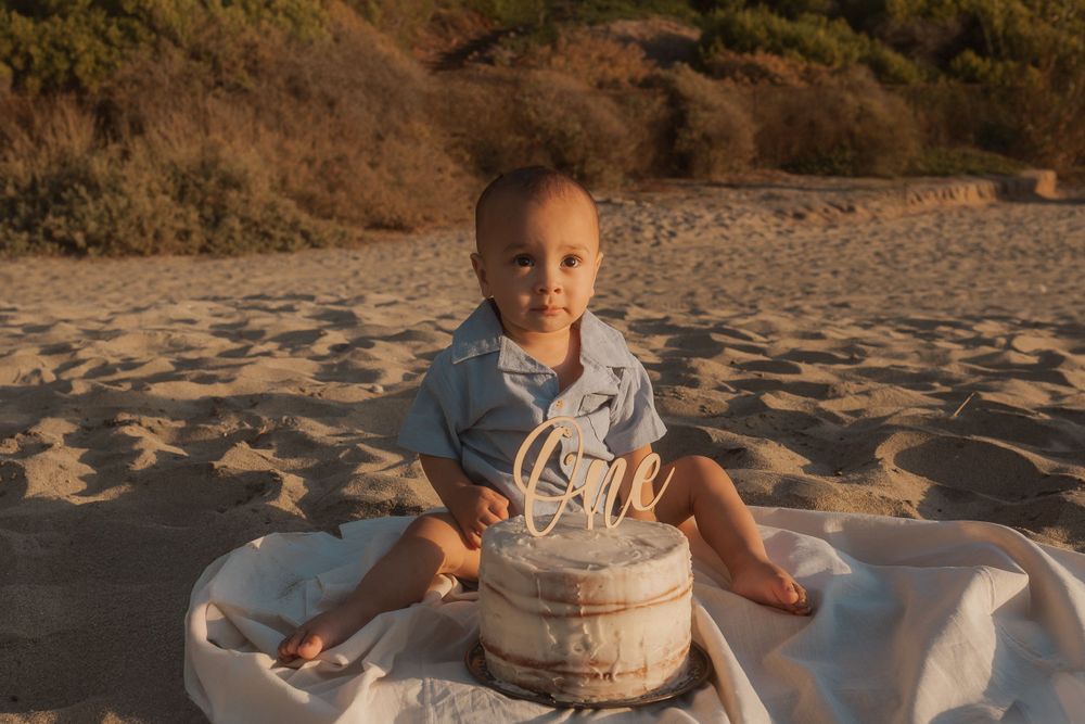 A one year birthday celebration on the beach with a smash cake during golden hour.