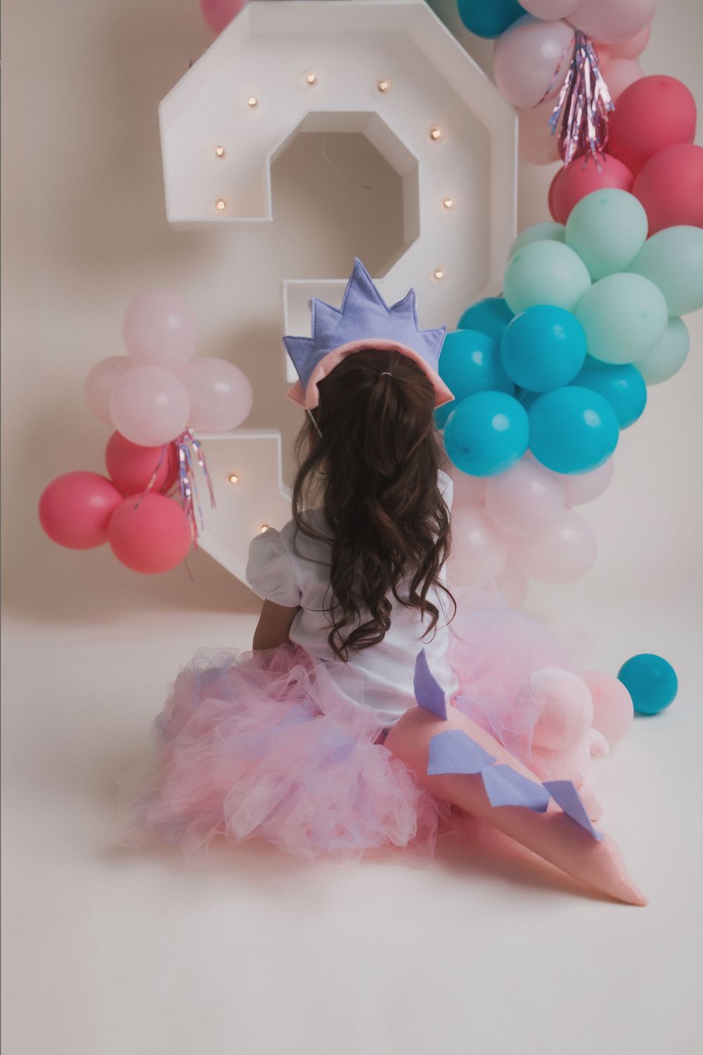 A birthday photoshoot setup with illuminated number 3 and pink and blue balloon garland.