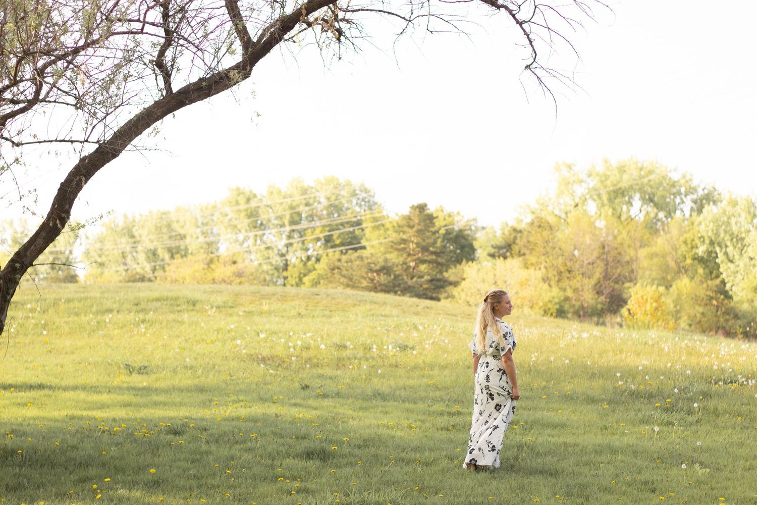 Person in a flowing dress stands alone in a sunny meadow.