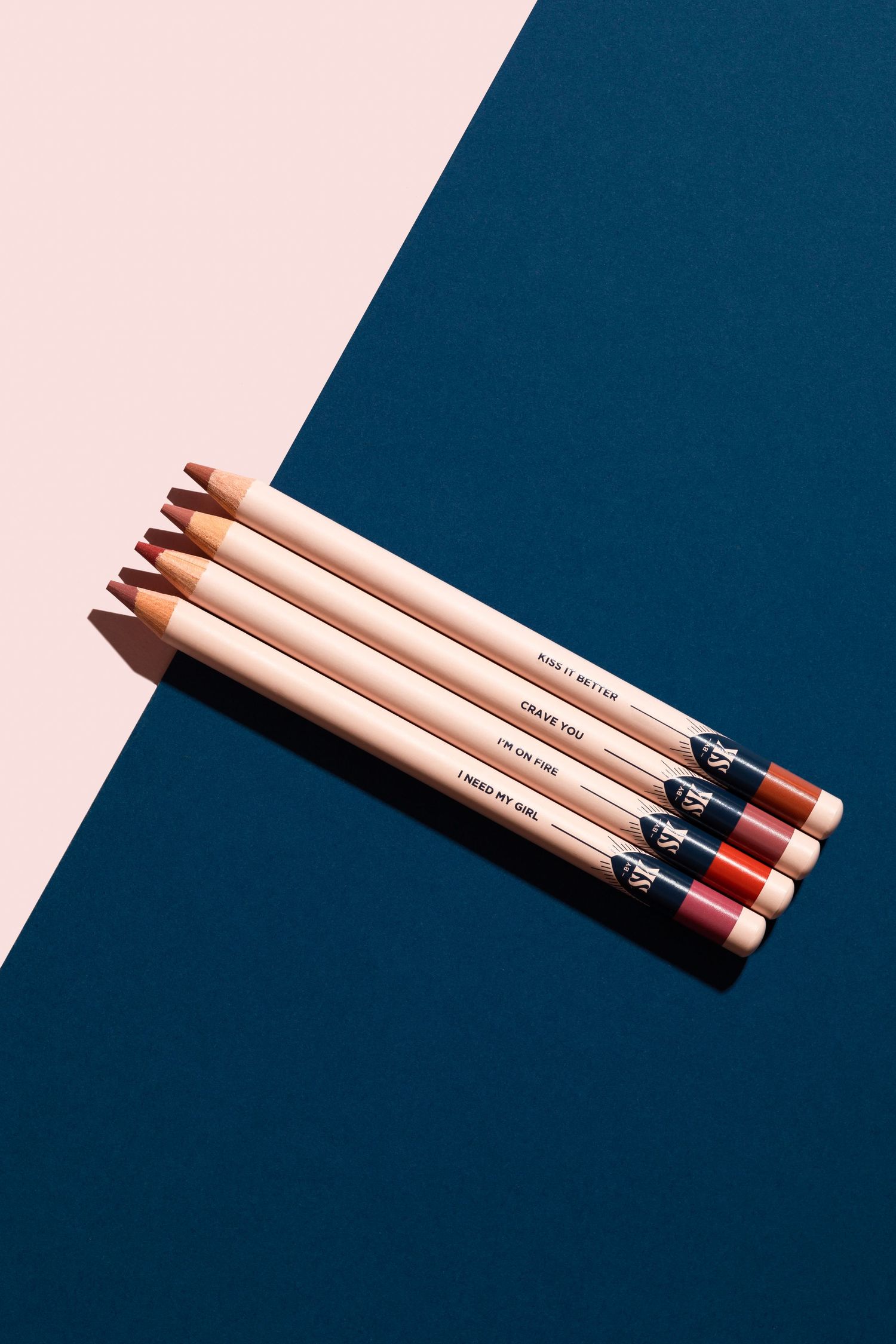 Lip Liner makeup pencils arranged in diagonal line against navy blue and baby pink split background.