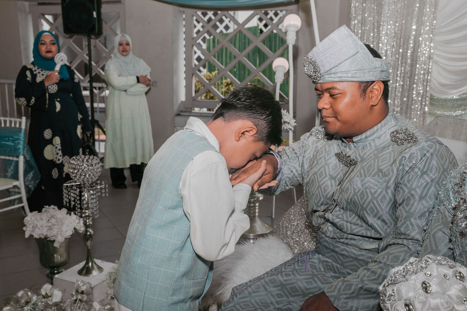 Cultural wedding ceremony ritual showing respect gesture in light blue and silver decorated setting.