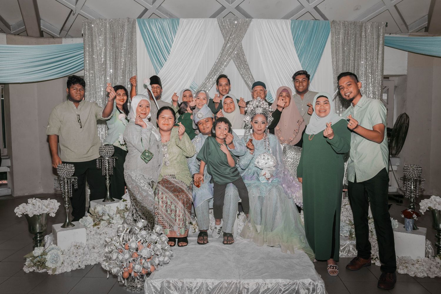 Large group photo of wedding party members in casual attire against white and turquoise backdrop.