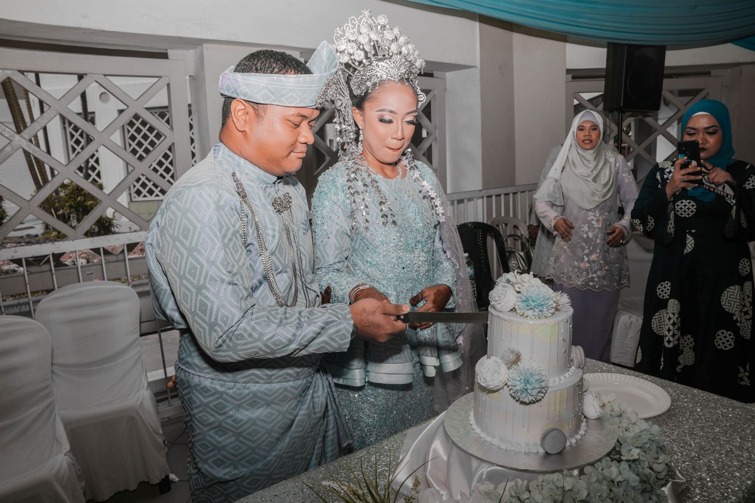 Couple cutting their white wedding cake during reception in elegant decorated venue.