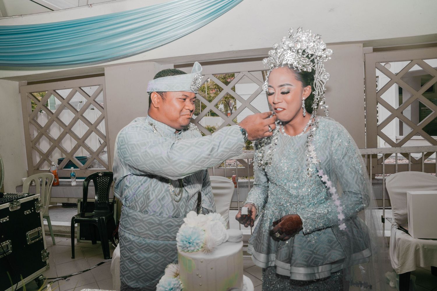 A ceremony where someone in silver attire is feeding cake at an elegant event with teal and white decor.