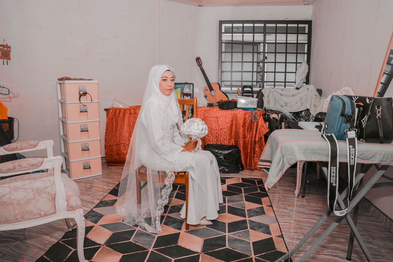 A bride in white sits in a room with orange accents and checkerboard flooring.