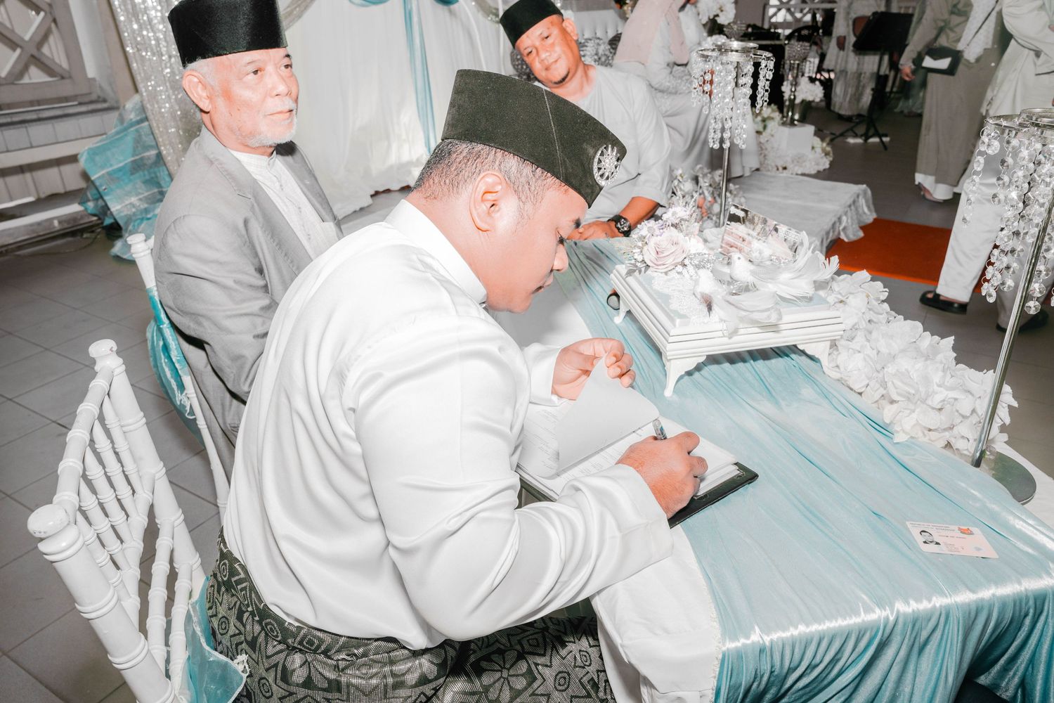 Officials in traditional dress signing documents at a blue-draped table.
