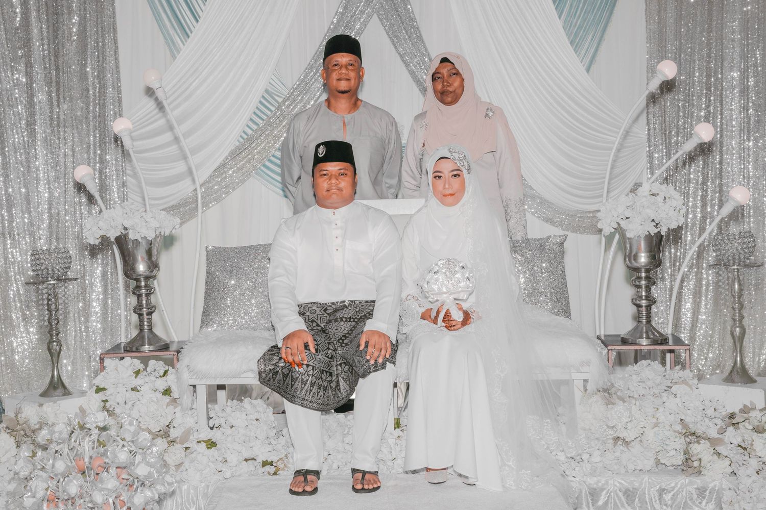 Wedding party portrait in white and silver decorated setting with traditional Malay attire.