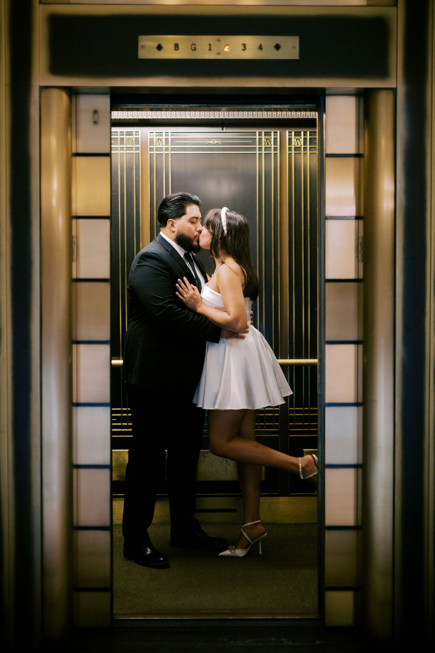 A romantic couple embraces in an Art Deco elevator with gold geometric patterns and warm lighting.