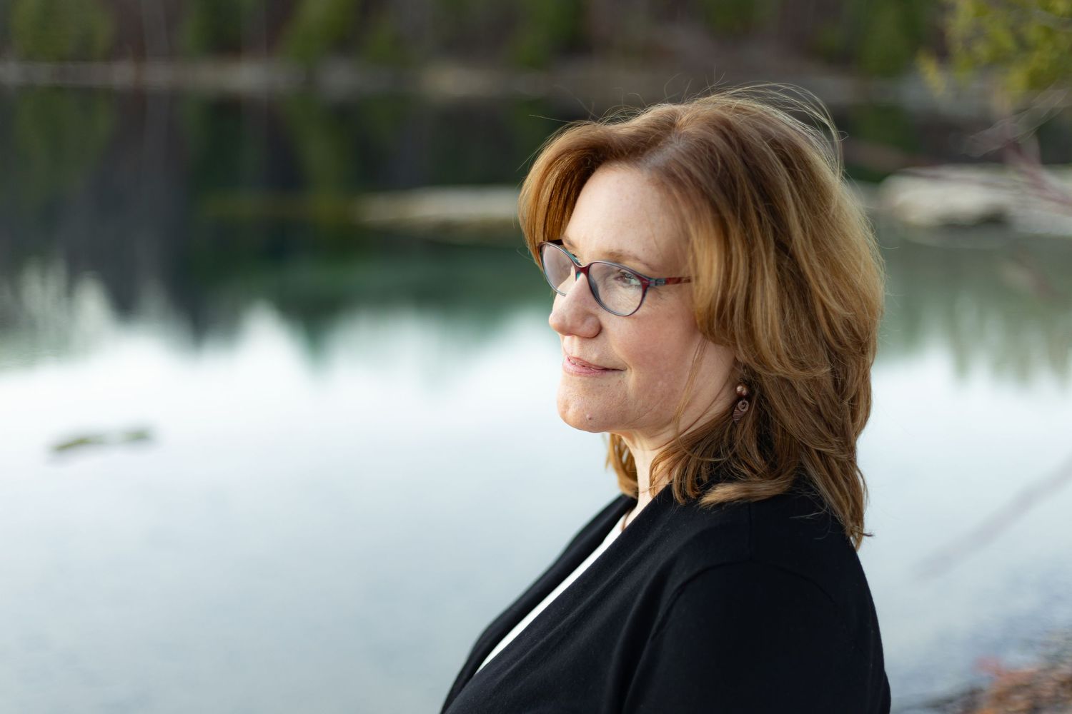 A professional portrait of a person in a white blazer sitting outdoors.