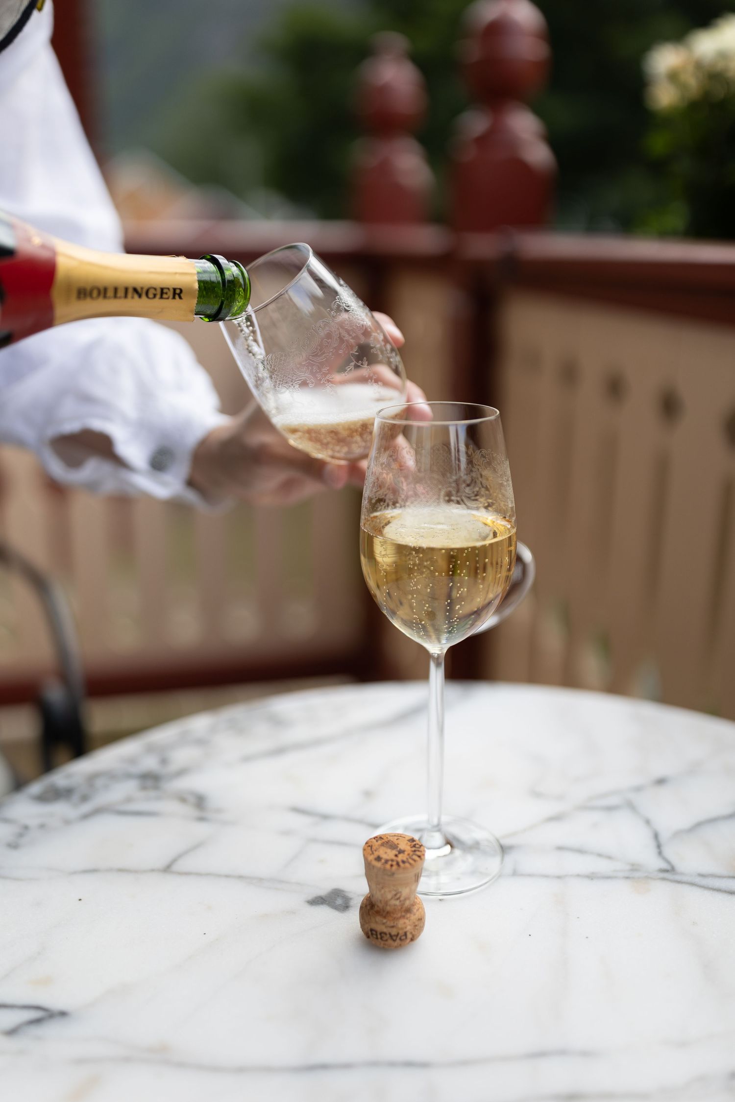 Bollinger champagne being poured into an elegant wine glass on a marble table with a cork.