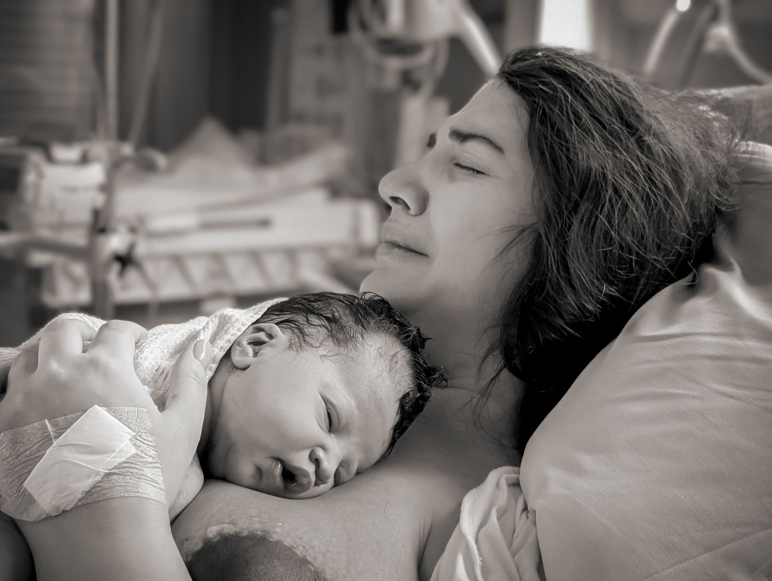Känslosam bild på en mamma med bebis på bröstet, hon gråter av lycka. Förlossningsfoto BB Solna Karolinska