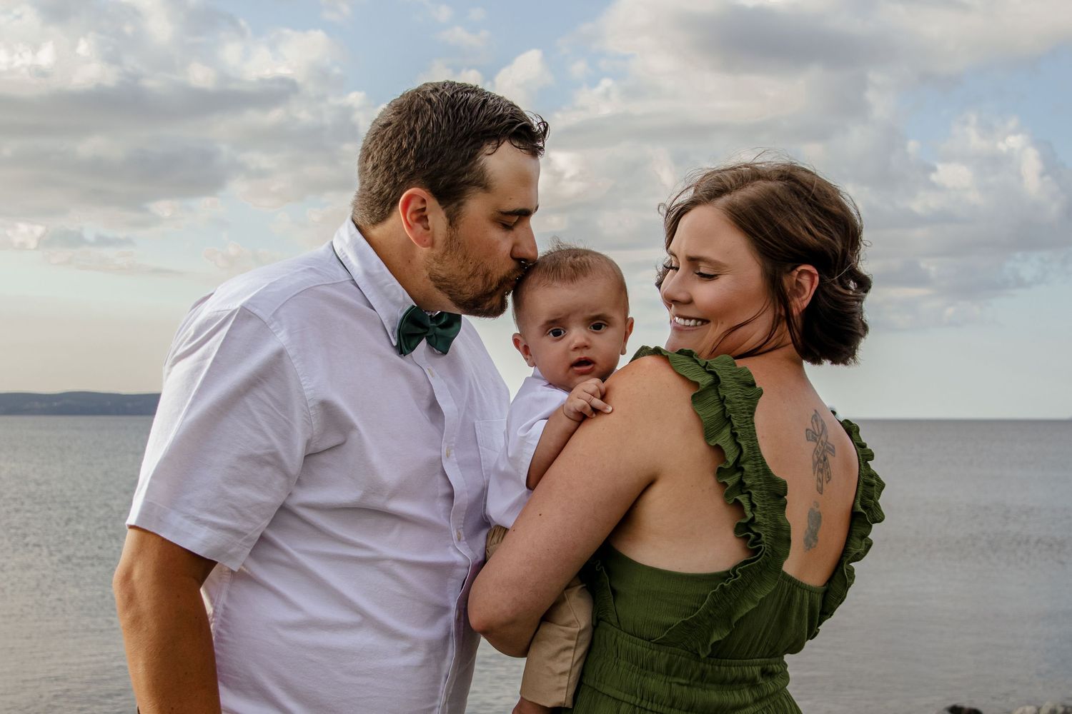 Family wearing white and green outfits share an intimate moment together by the ocean at sunset.