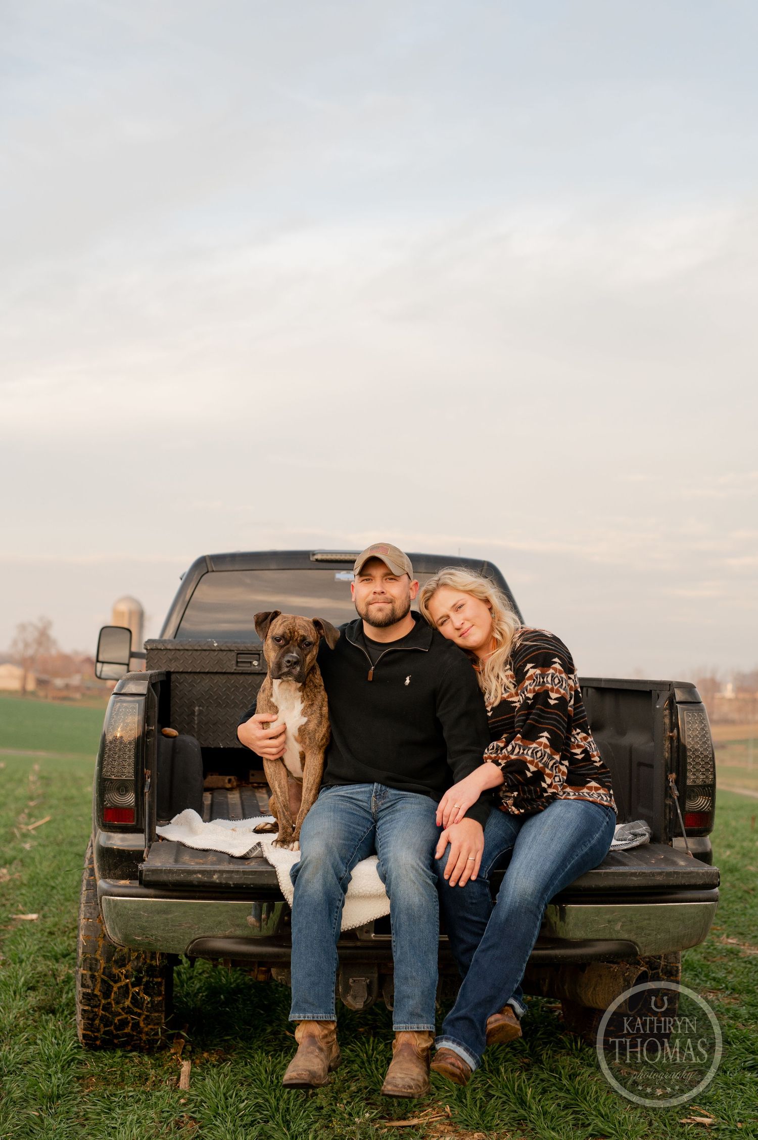 A couple relaxes on their pickup truck tailgate with their dog in a rural setting.