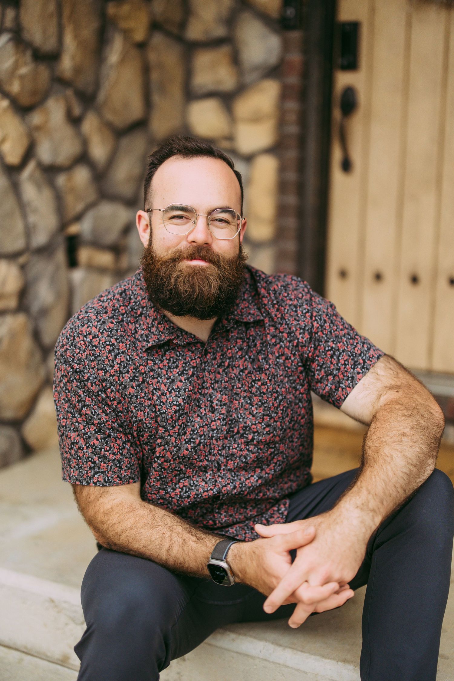 Casual portrait of bearded man in floral print shirt sitting on stone steps.