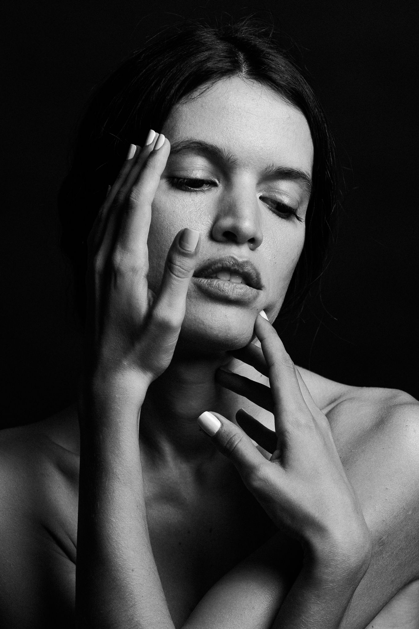 Artistic black and white beauty portrait with dramatic lighting showing hands touching face and closed eyes.