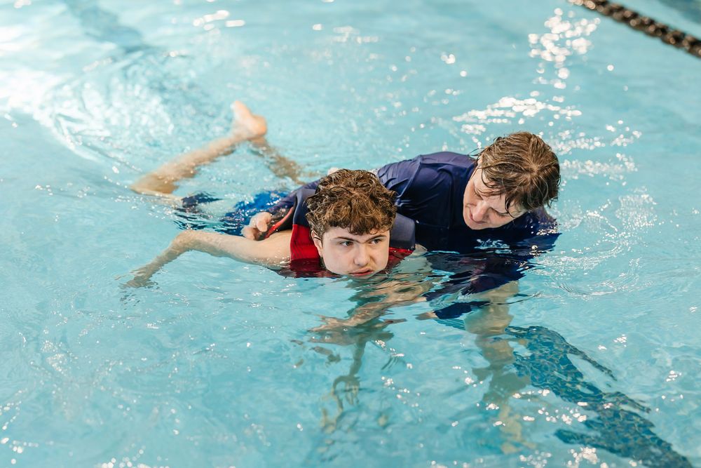 Students practice floating on their backs in a swimming pool during a water safety lesson.