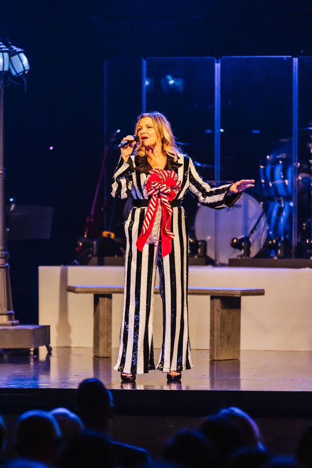 A performer in a black and white striped outfit sings passionately on stage during a theatrical production.