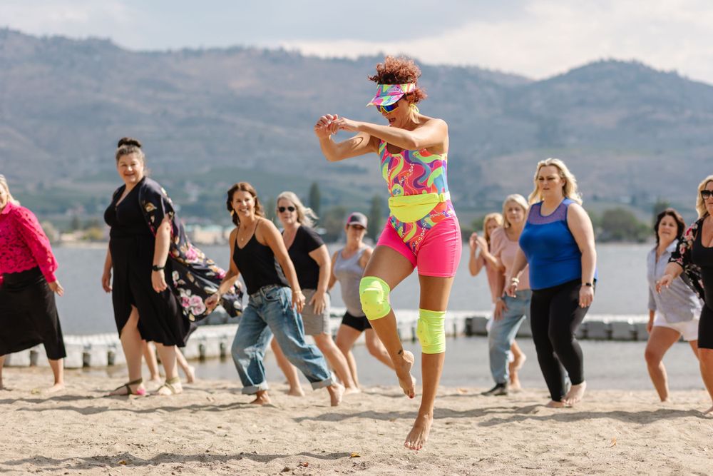 Beach fitness class participants jumping in unison with mountains behind them.
