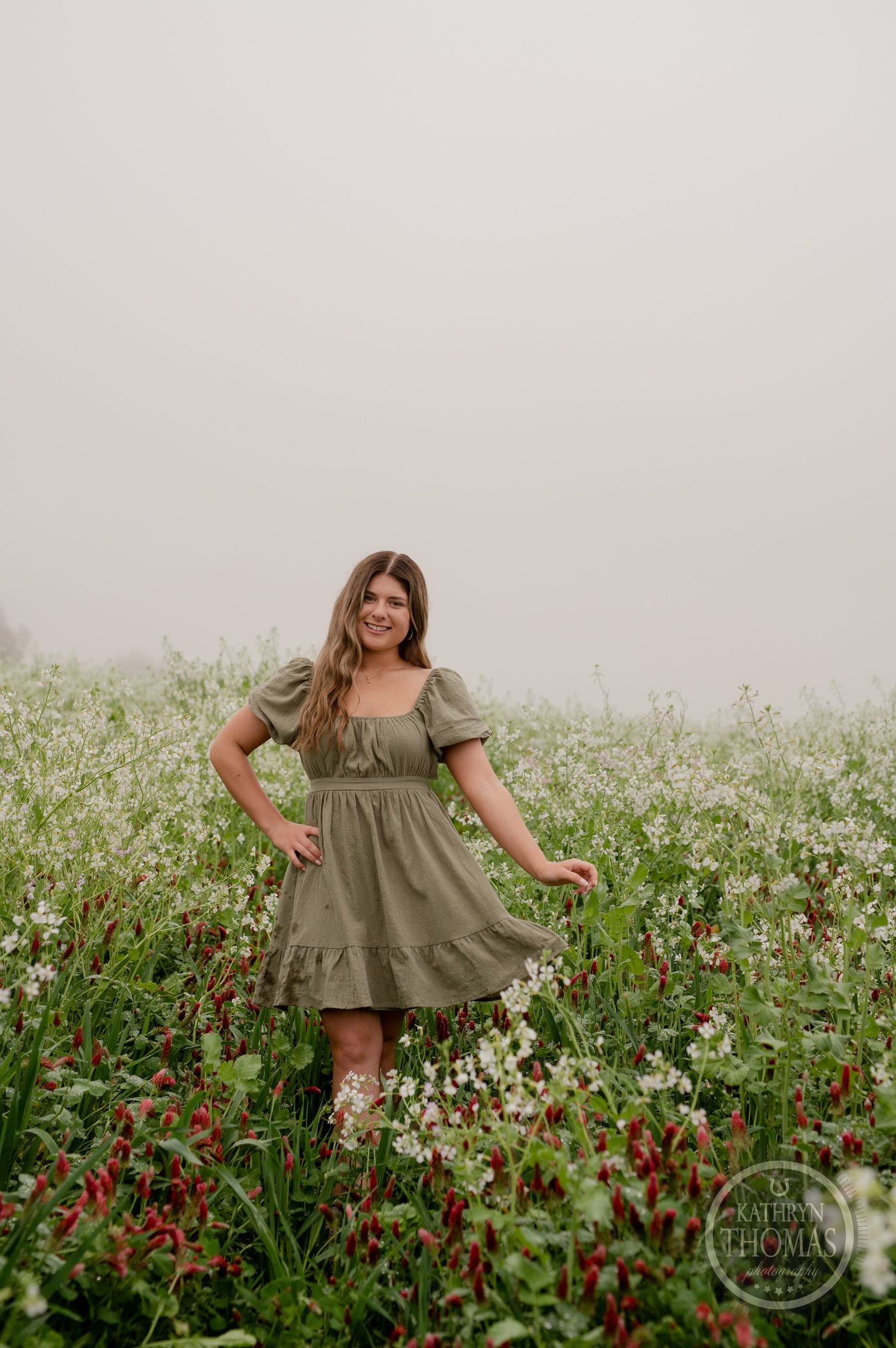 A countryside portrait showing someone in a green peasant dress standing among blooming wildflowers.