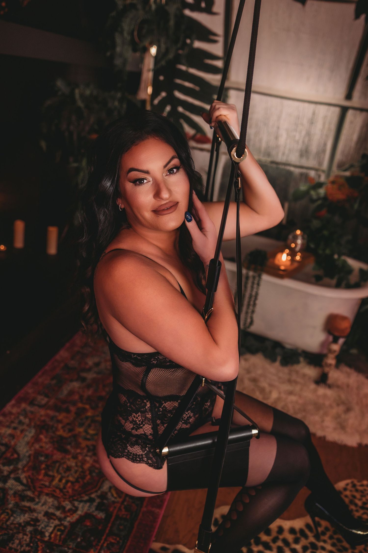 A boudoir photoshoot on a swing featuring black lace lingerie and soft ambient lighting.