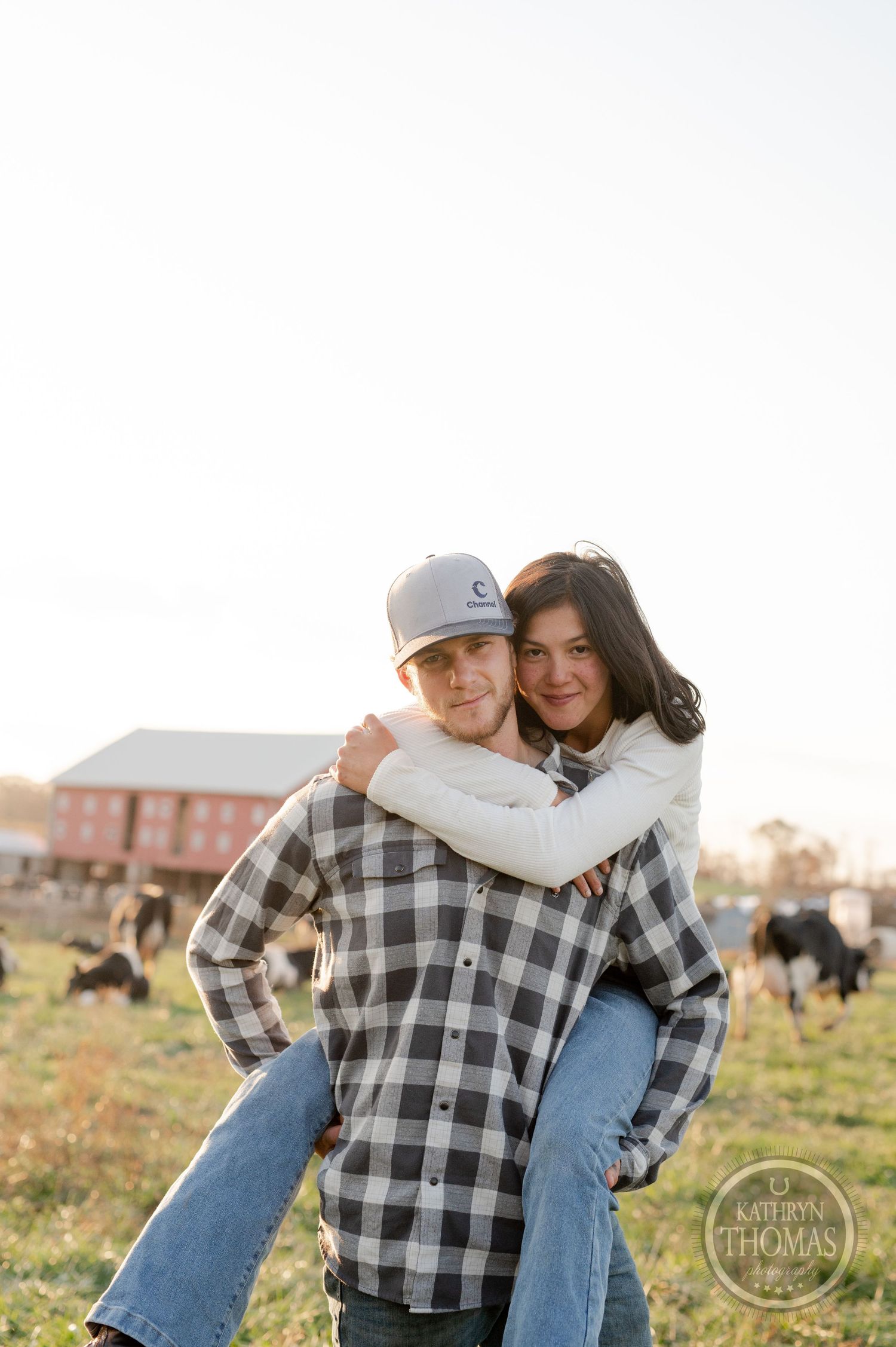 A joyful piggyback pose against a bright farm backdrop with livestock in the distance.