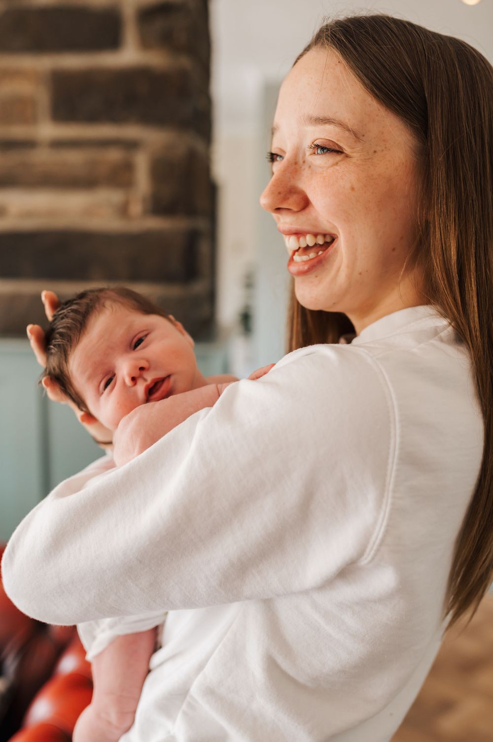 A tender moment between parent and newborn baby as they share smiles in front of a brick wall.