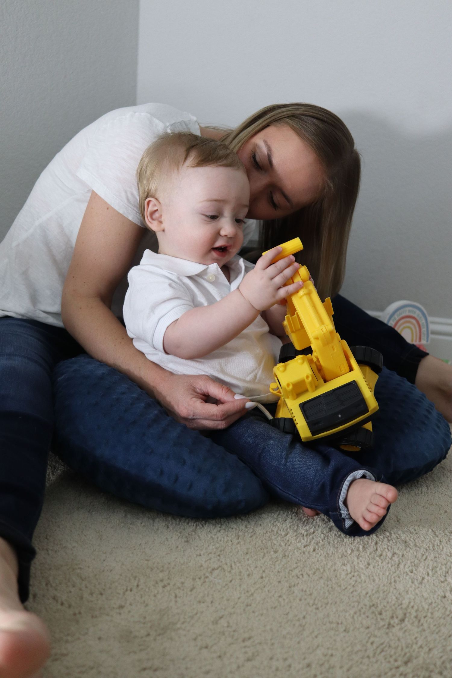 Young mother sitting on carpet playing with baby and yellow toy construction truck.