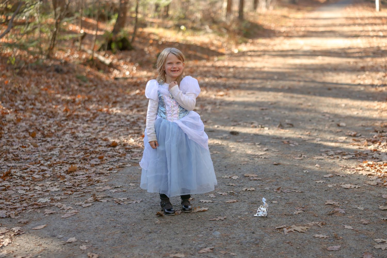 Young girl in white princess dress standing on autumn woodland path.