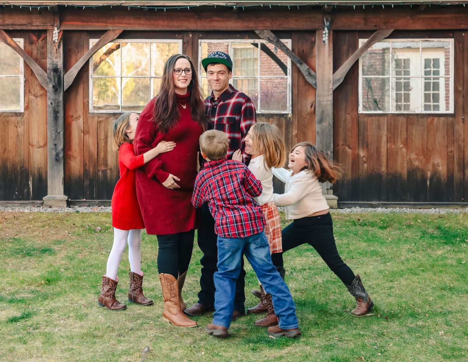 Family with four children hugging parents outside rustic barn.