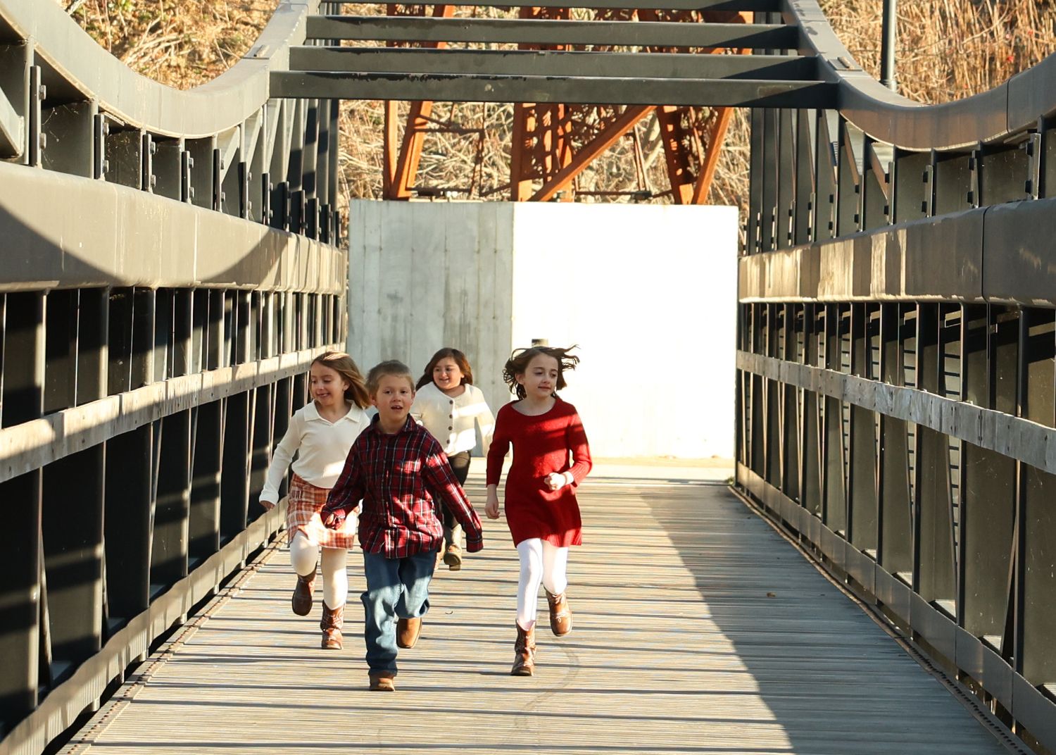 Four children running joyfully across a pedestrian bridge.