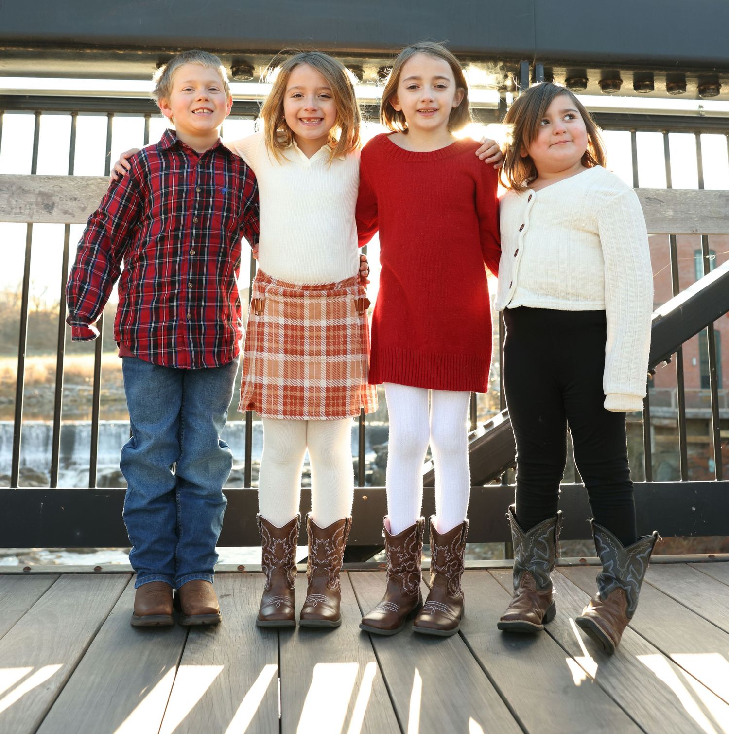 Four children in holiday outfits smiling together on outdoor deck.