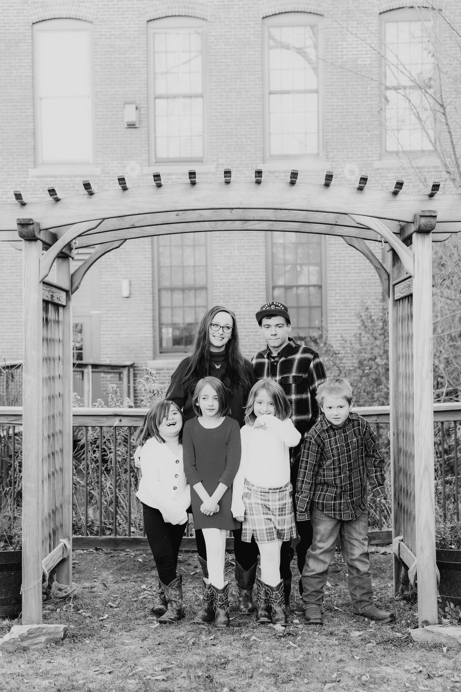 Black and white family portrait of parents with four children under garden arch.