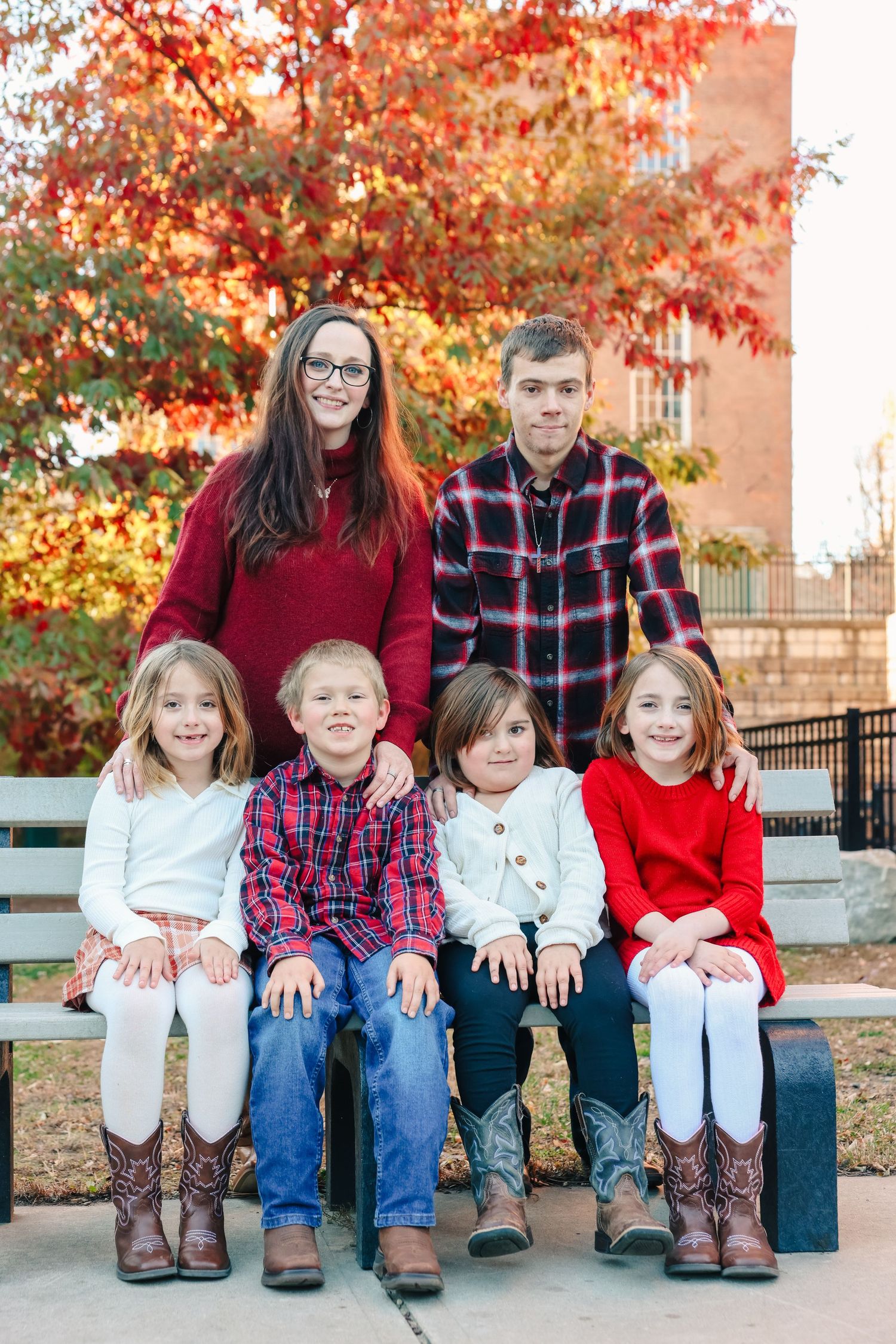 Family of six posing on a bench surrounded by colorful fall trees in autumn.