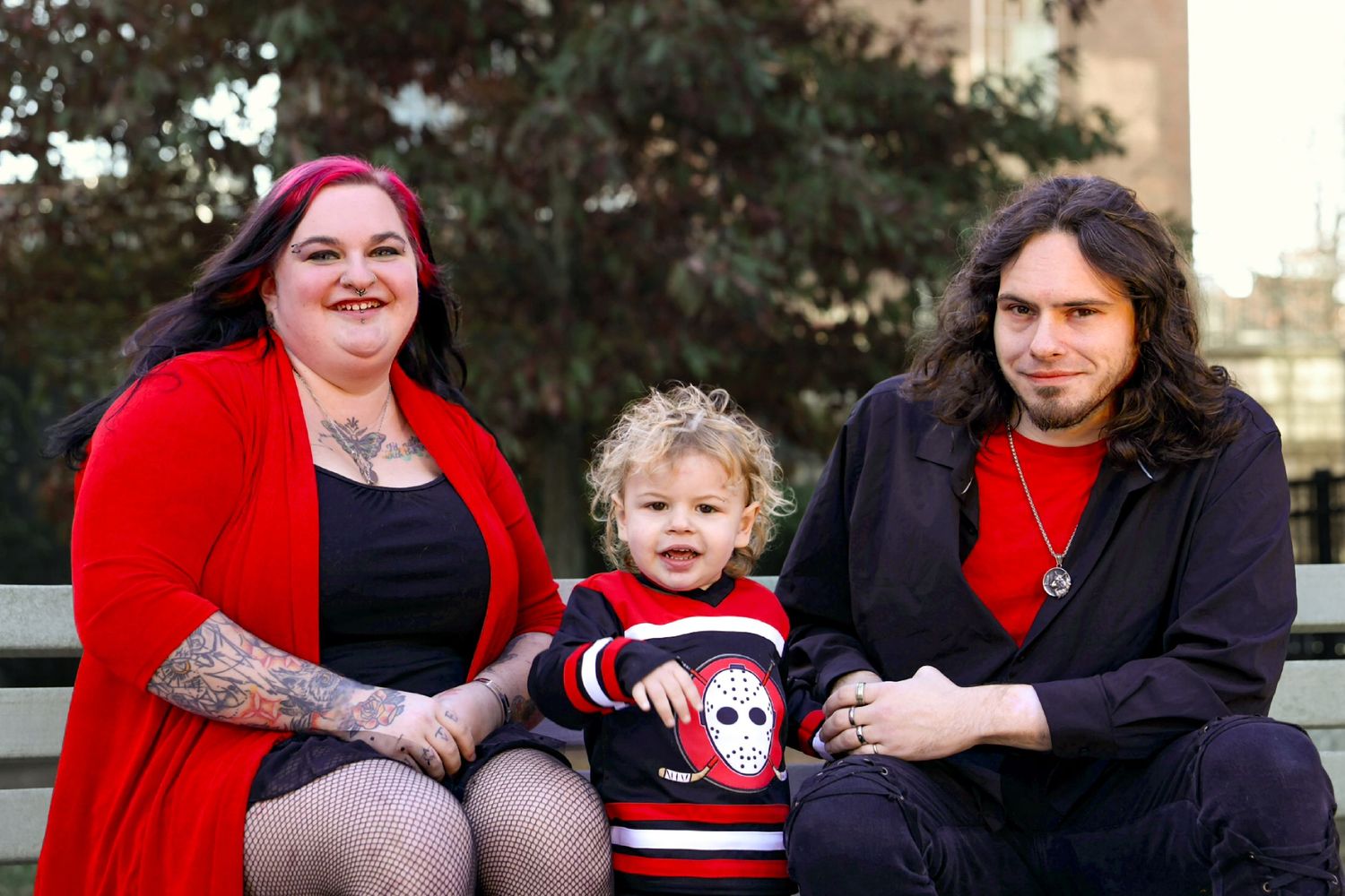 Family portrait with tattooed mother, toddler, and father in red outfits outdoors.