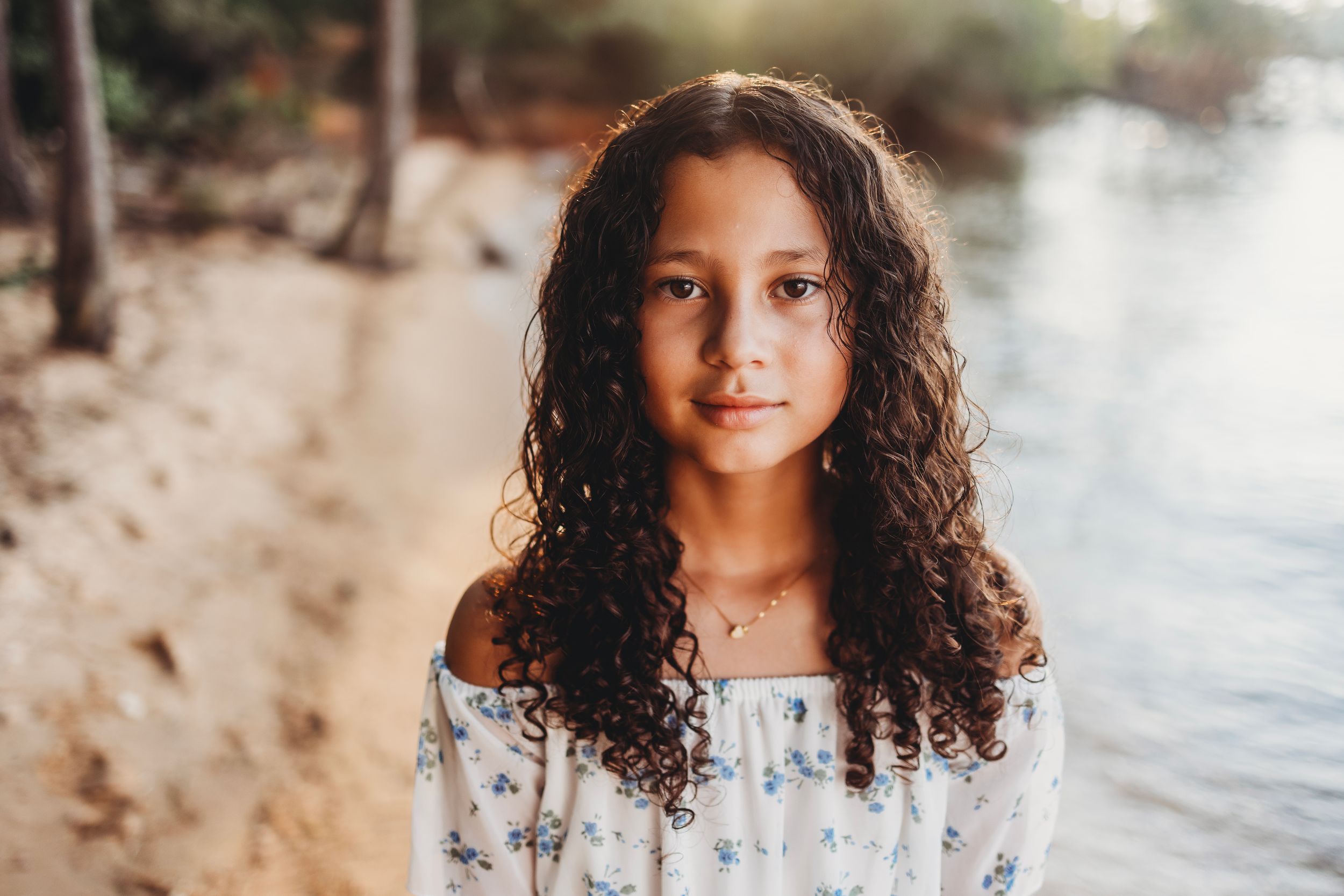 Portrait of a young person in a floral dress by the water during golden hour.