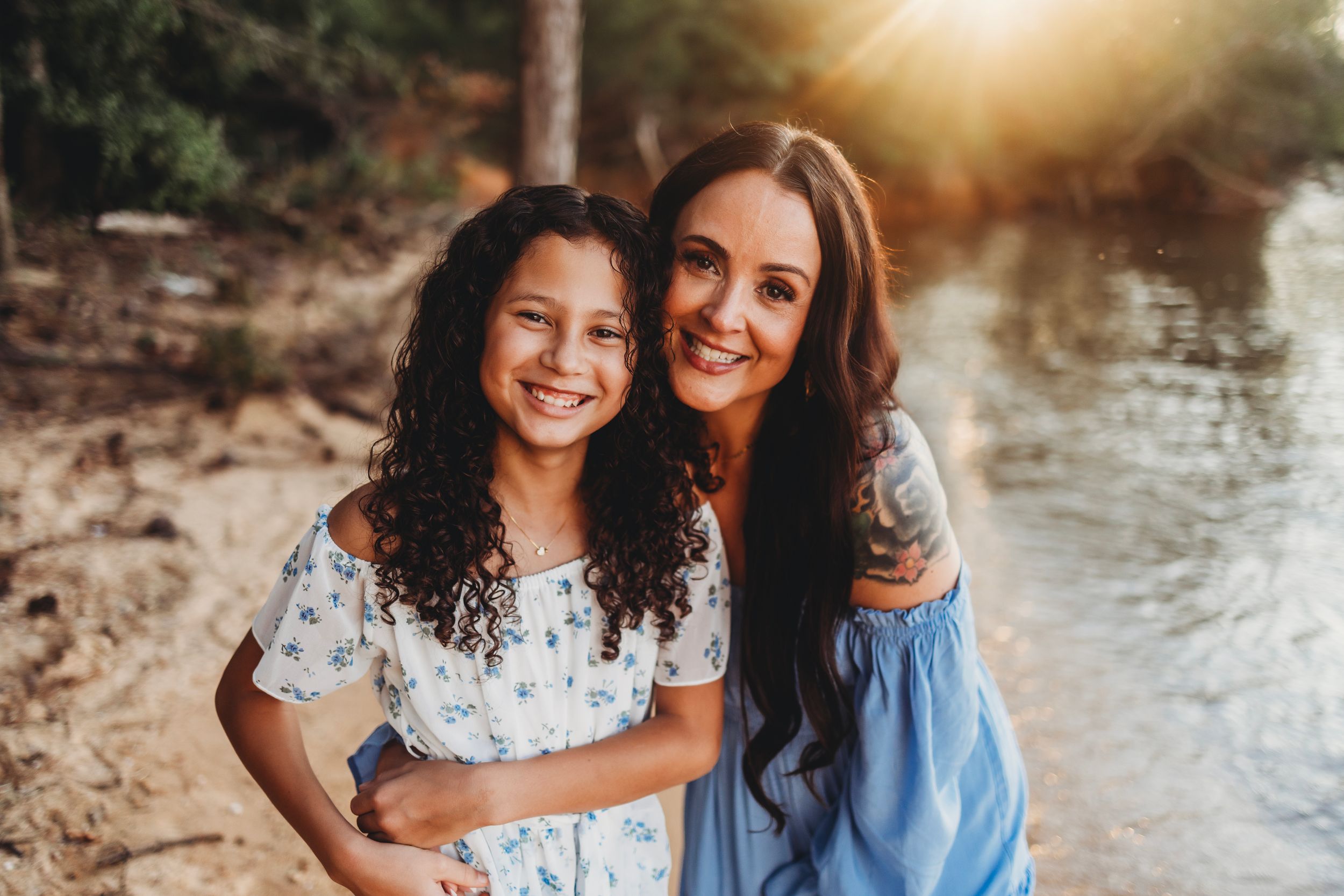 Two people embracing and smiling by a lake during golden hour sunset.