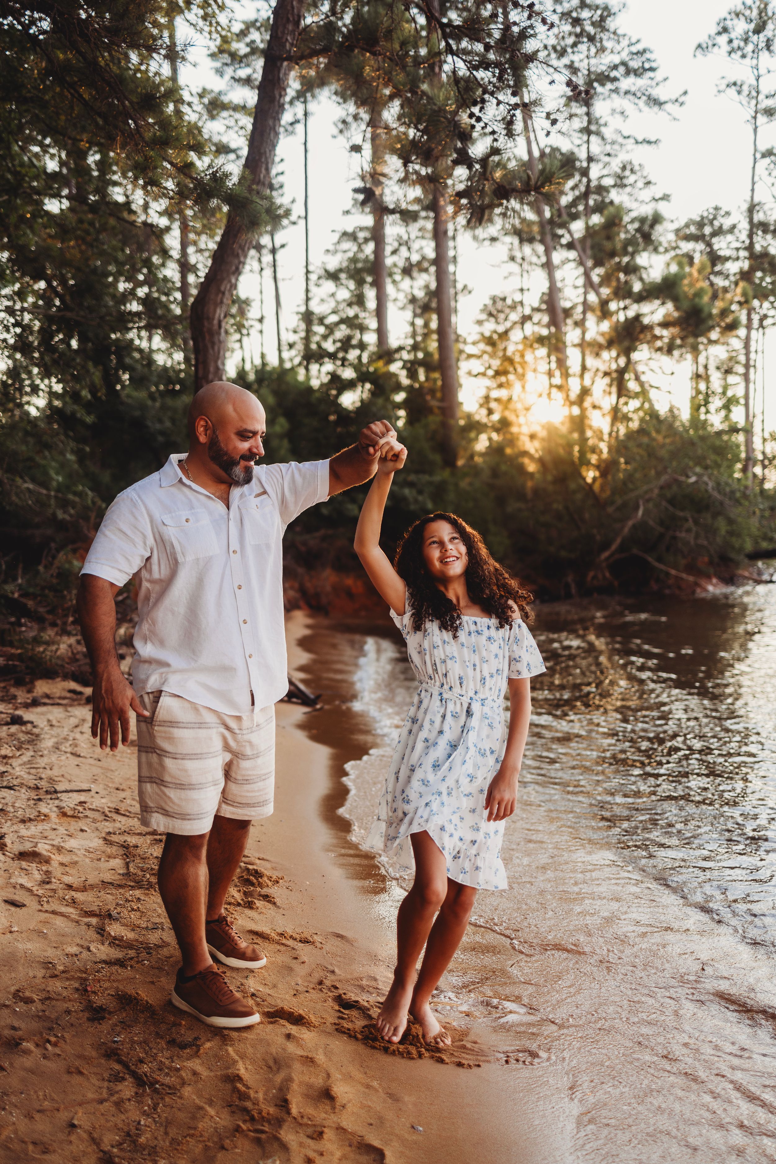 A candid lakeside dance moment at sunset with pine trees in the background.