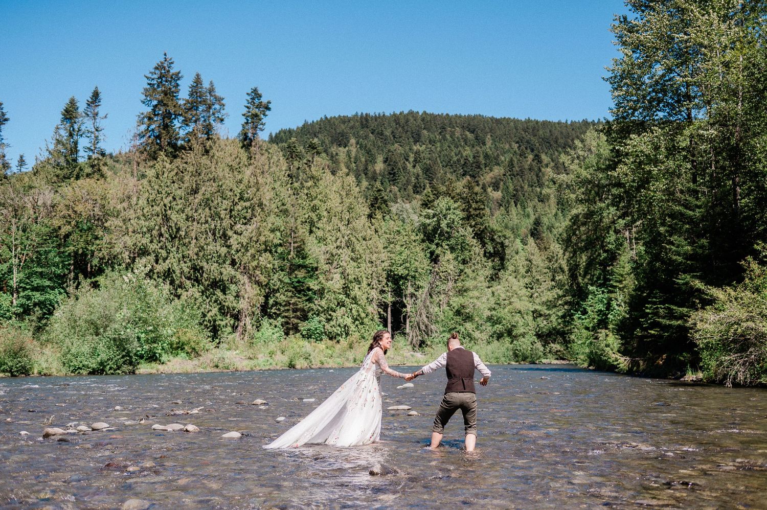 couple walk through the Dungeness River on their elopement day. Photo by Pine + Vow