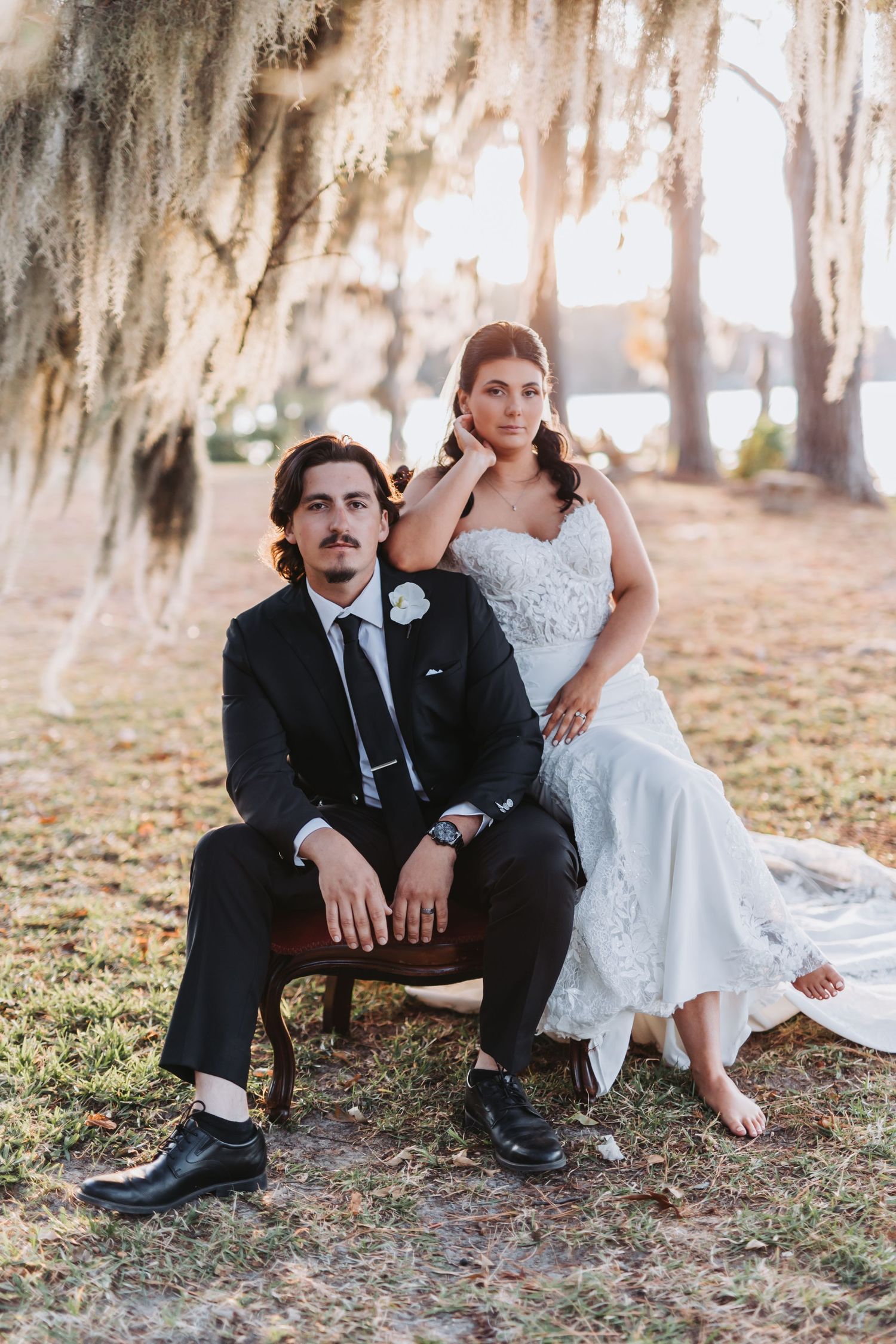 A wedding couple poses under Spanish moss draped trees at sunset in a romantic outdoor setting.