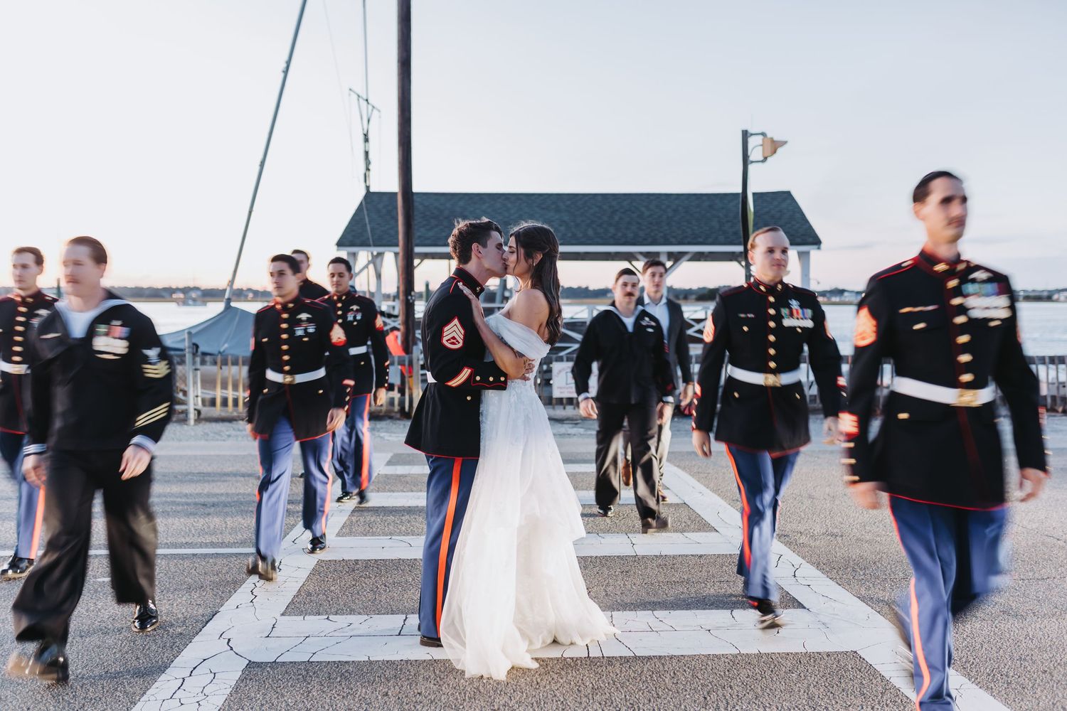 Wedding party walks along a beachfront pier during sunset creating silhouettes against the ocean backdrop.